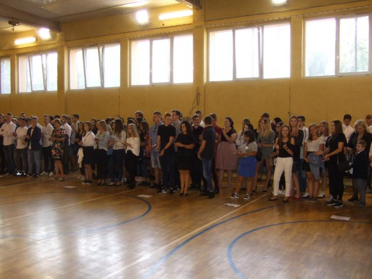 Na zdjęciu duża grupa uczniów w strojach galowych podczas rozpoczęcia roku szkolnego w sali gimnastycznej
